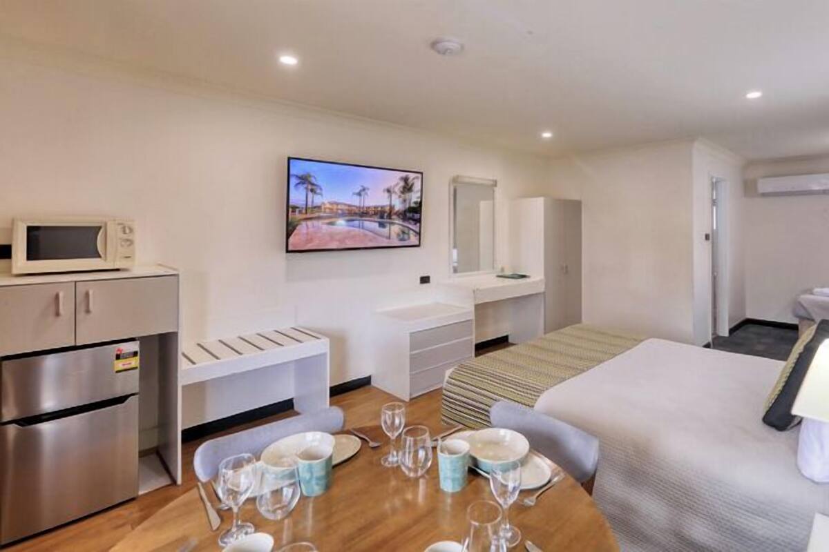 A modern hotel room with a kitchenette, a dining area, a bed, and a TV.
