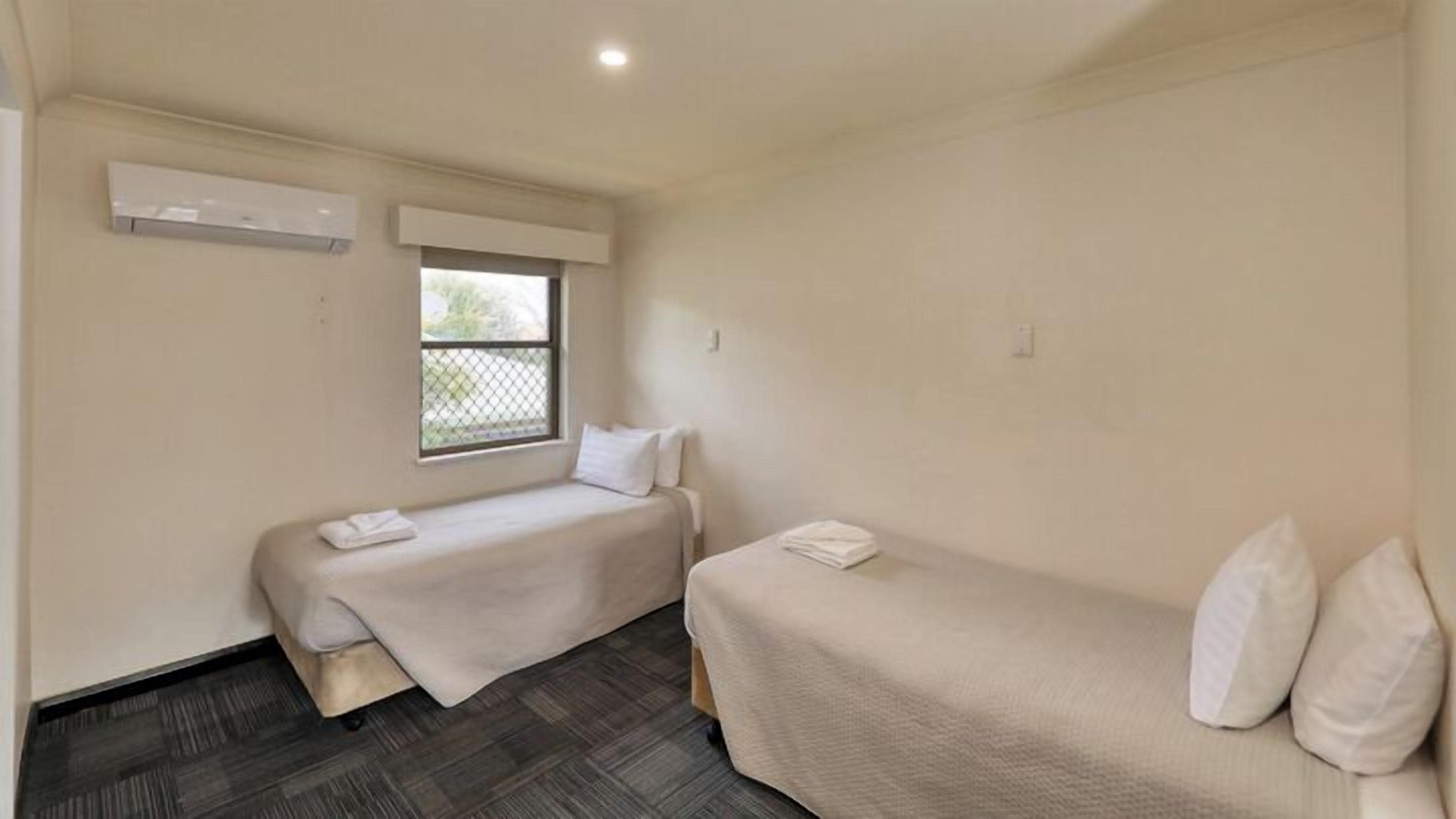 Una habitación pequeña y limpia con dos camas individuales, una ventana con vistas y un aire acondicionado de pared.