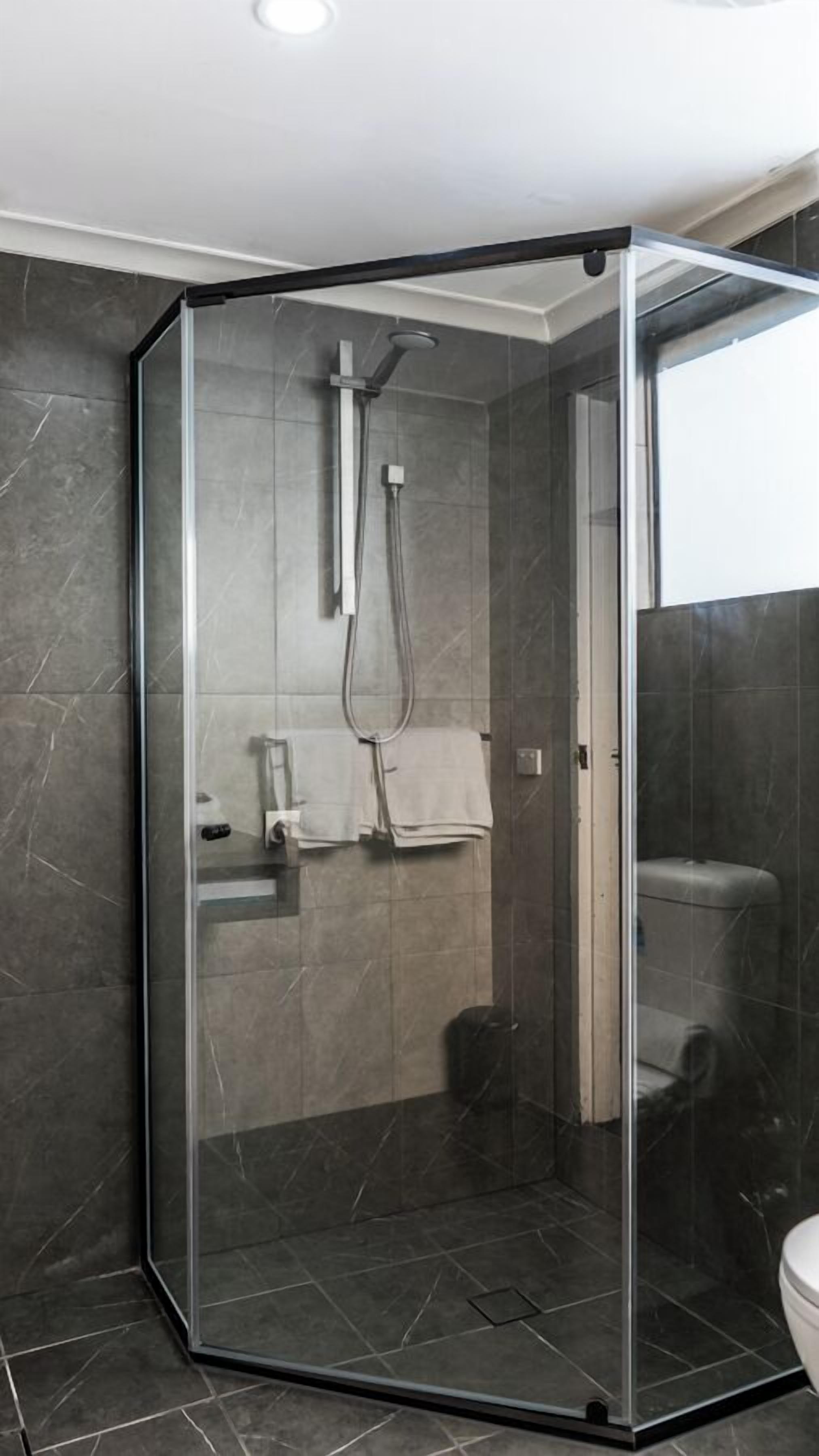 A modern shower enclosure with a glass door, a handheld showerhead, and a towel rack.