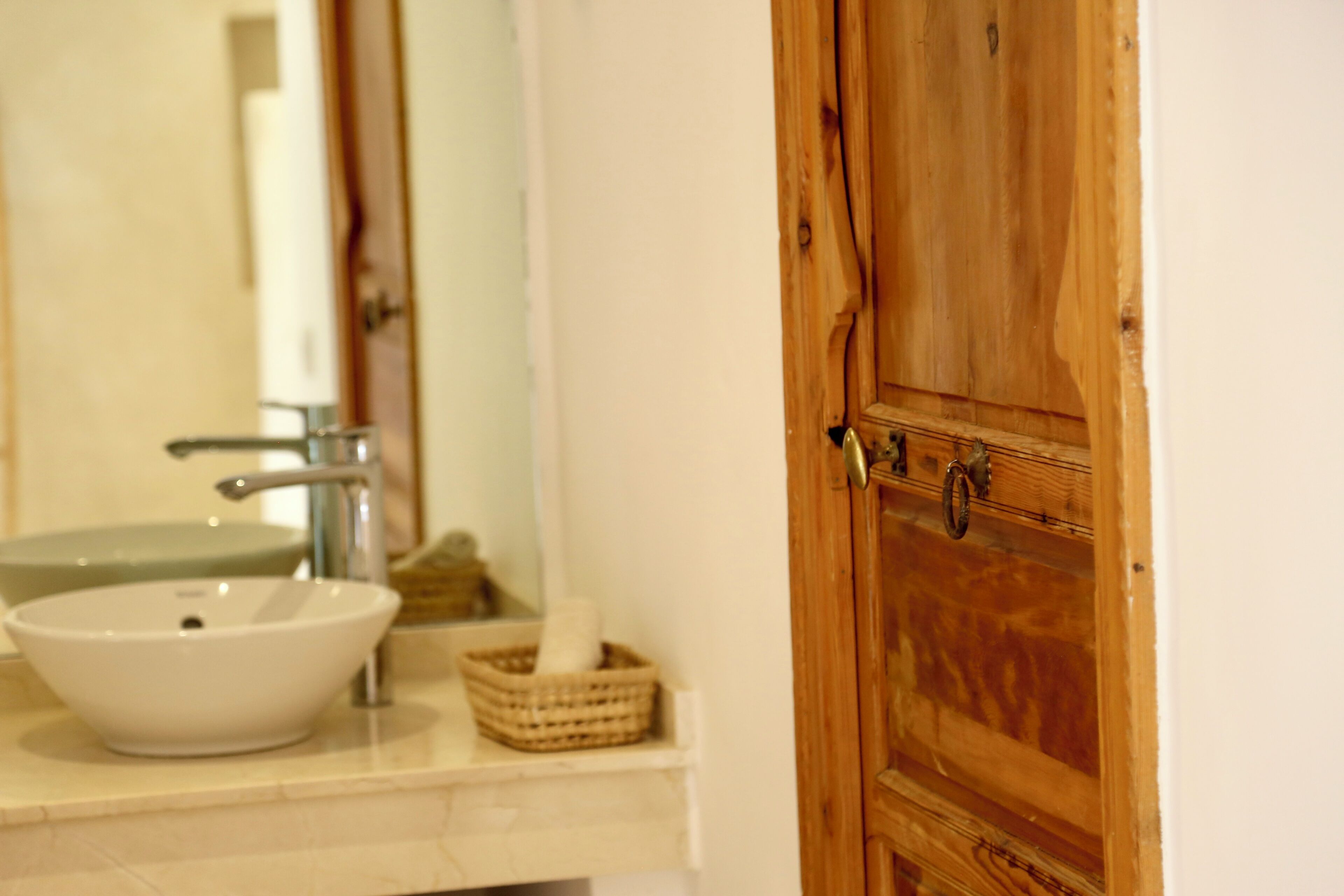 Un baño con lavamanos blanco, puerta de madera y espejo.