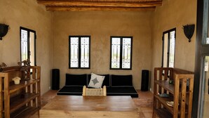 Una stanza con pavimento in legno, un divano, un tavolo di legno e due finestre con inferriate.
