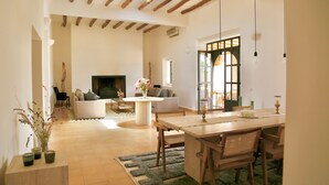 Un ampio soggiorno con camino, una zona pranzo con arredi in legno e vista sull'esterno attraverso una grande finestra.
