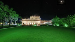 A two-story building with a balcony, surrounded by a well-lit lawn and palm trees. - Shiv Tirth By 97 Royal Vista  (Mawal)