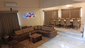 A spacious living room with a sectional sofa, a coffee table, and a dining area with a table and chairs. - Shiv Tirth By 97 Royal Vista  (Mawal)