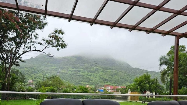 A covered outdoor seating area with black leather sofas and a view of a mountainous landscape. - Shiv Tirth By 97 Royal Vista  (Mawal)