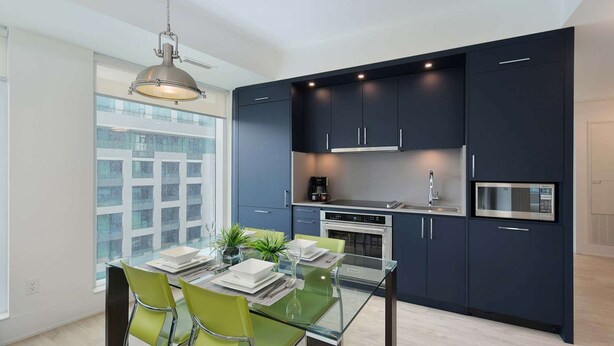 A modern kitchen with dark cabinets, a glass dining table, and a hanging light fixture. - 2 Bedroom/2 Bathroom Suite (Toronto)