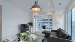 A modern living room with a glass coffee table, a sofa, a TV, and a dining area with a glass table and chairs. - 2 Bedroom/2 Bathroom Suite (Toronto)