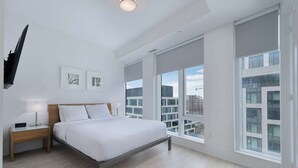 A modern hotel room with a large bed, bedside tables, and a city view. - 2 Bedroom/2 Bathroom Suite (Toronto)