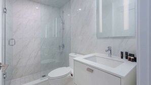 Une salle de bain moderne avec une douche à parois de verre, des toilettes blanches et un meuble-lavabo avec des articles de toilette.