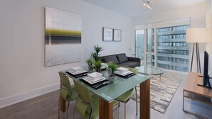 Un salon moderne avec une table à manger en verre, des chaises vertes, un canapé gris et une grande fenêtre donnant sur la ville.