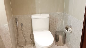 A small, modern bathroom with a toilet, a shower, and a trash can.