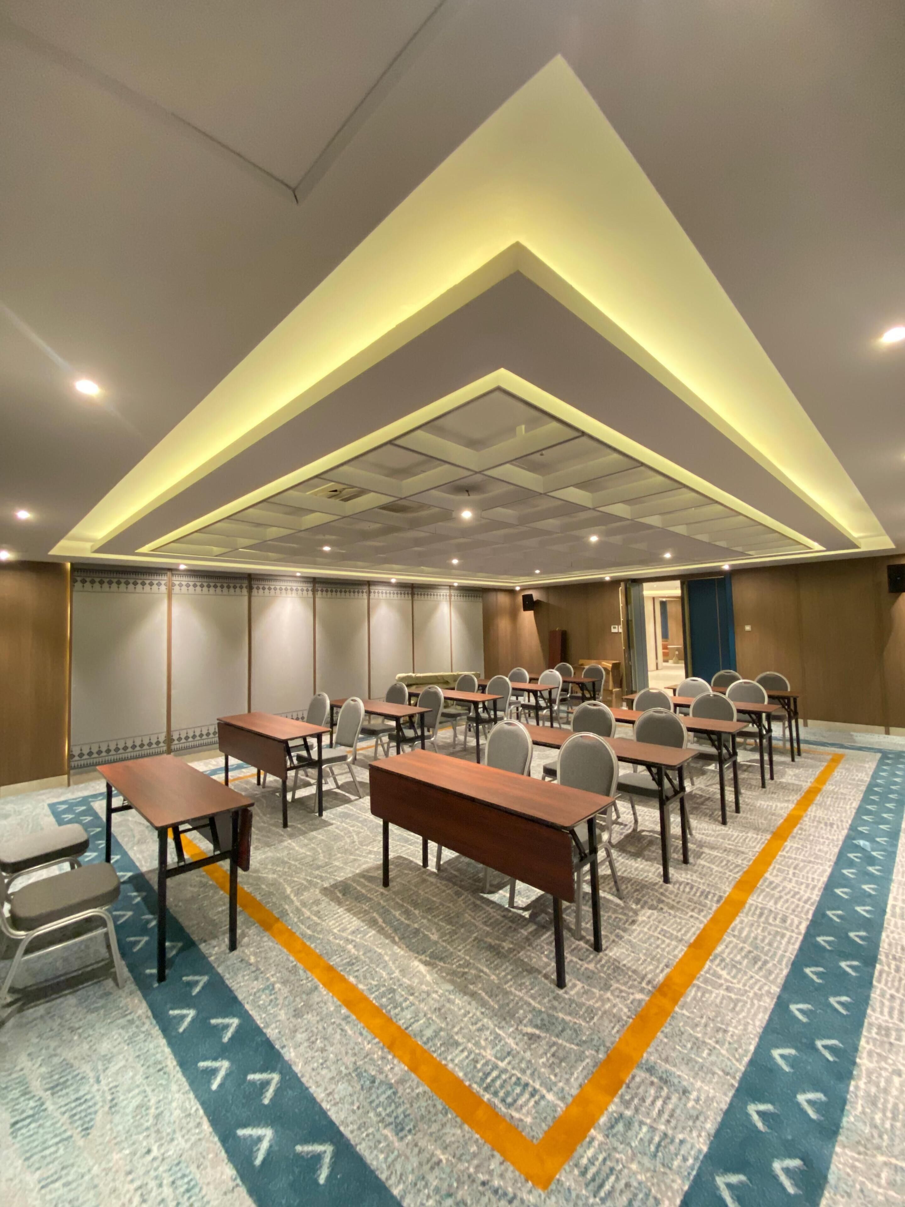 A conference room with multiple tables and chairs, a patterned carpet, and a ceiling with recessed lighting.