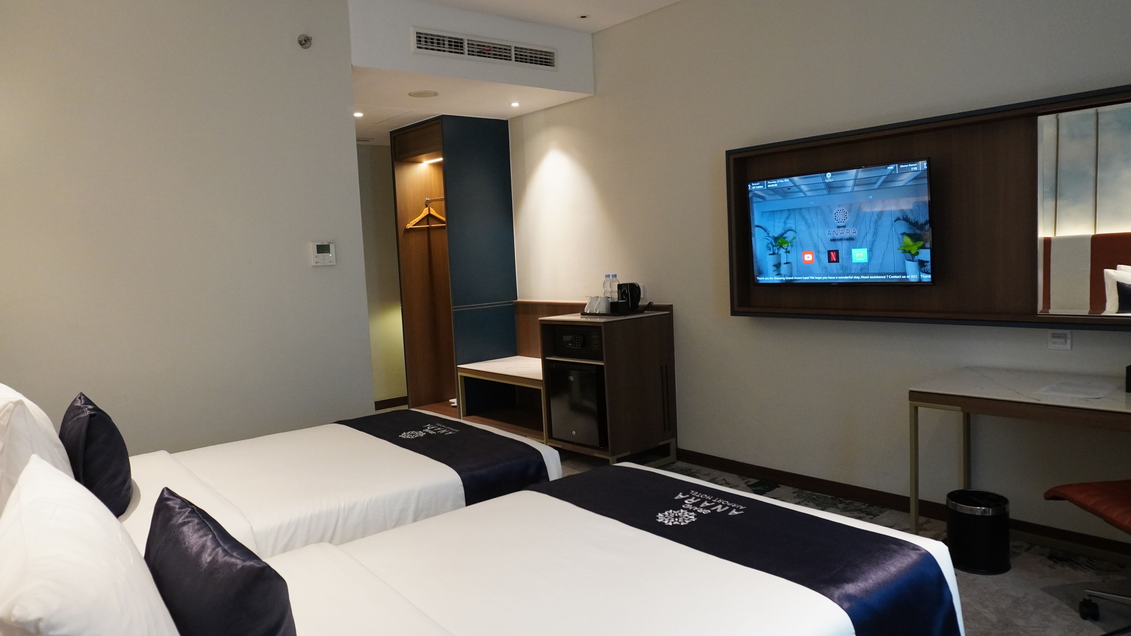 Habitación de hotel con dos camas, un escritorio, un televisor y un armario.