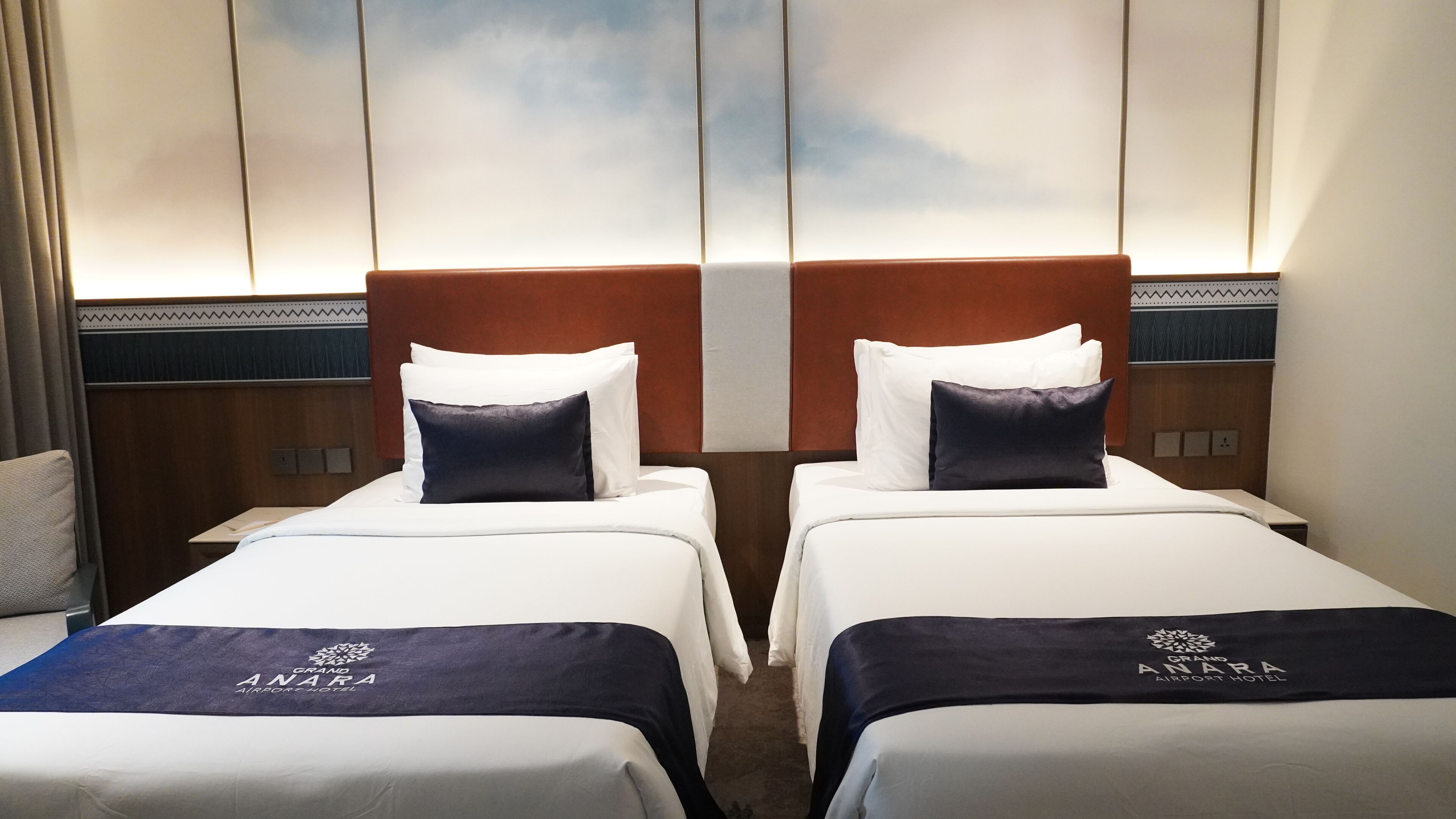 Habitación de hotel con dos camas, cada una con sábanas blancas y cabeceros azul oscuro.