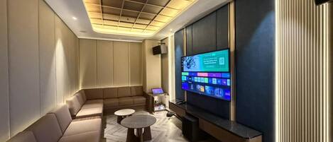 A modern living room with a large flat-screen TV, a sofa, two small tables, and a decorative ceiling.