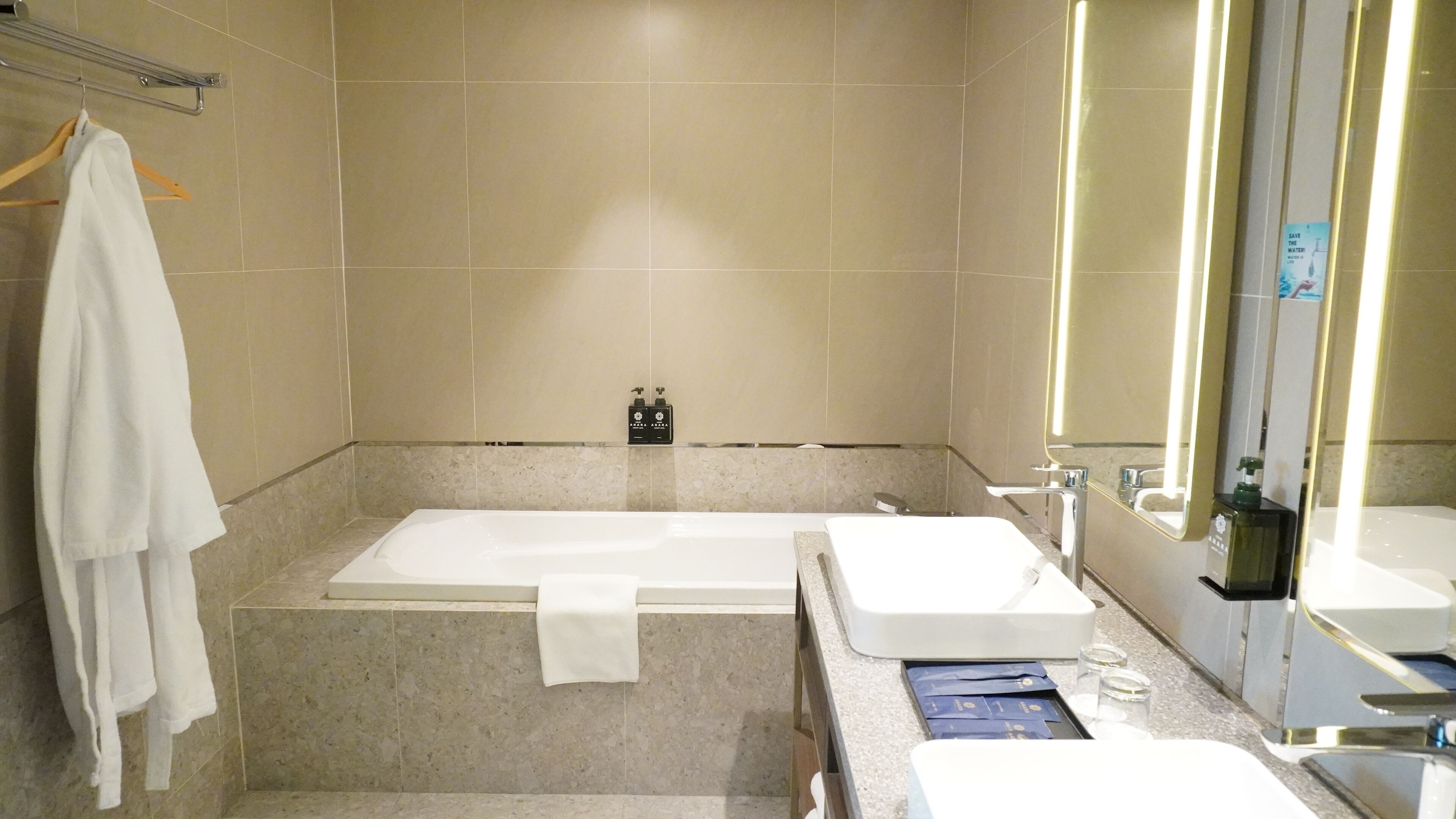 A modern bathroom with a bathtub, two sinks, a towel rack, and a mirror.