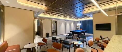Un área de lounge moderna con mesa de billar, asientos cómodos y una recepción de mármol.