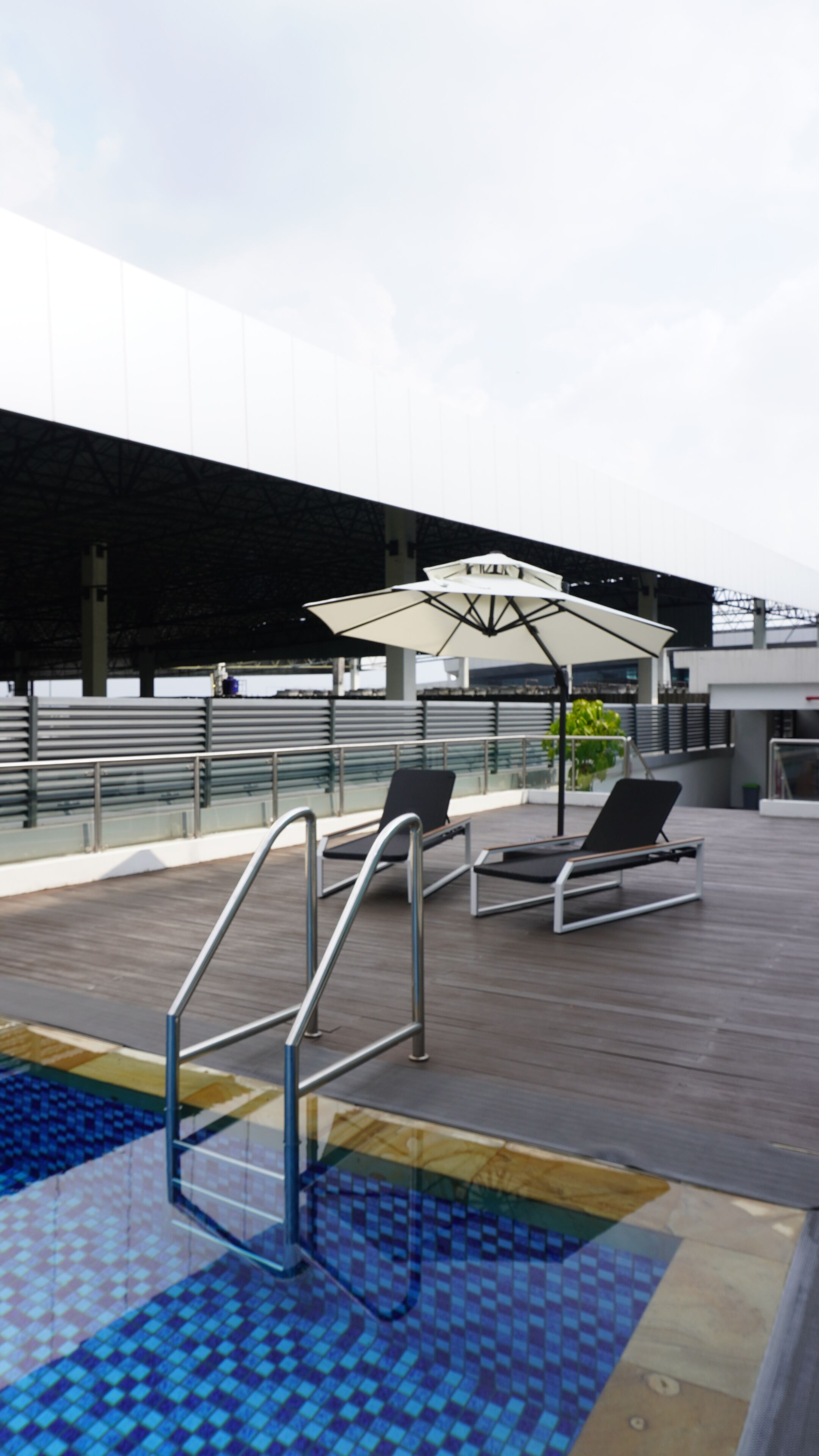 Un área de piscina en la azotea con sillones de descanso y sombrillas.