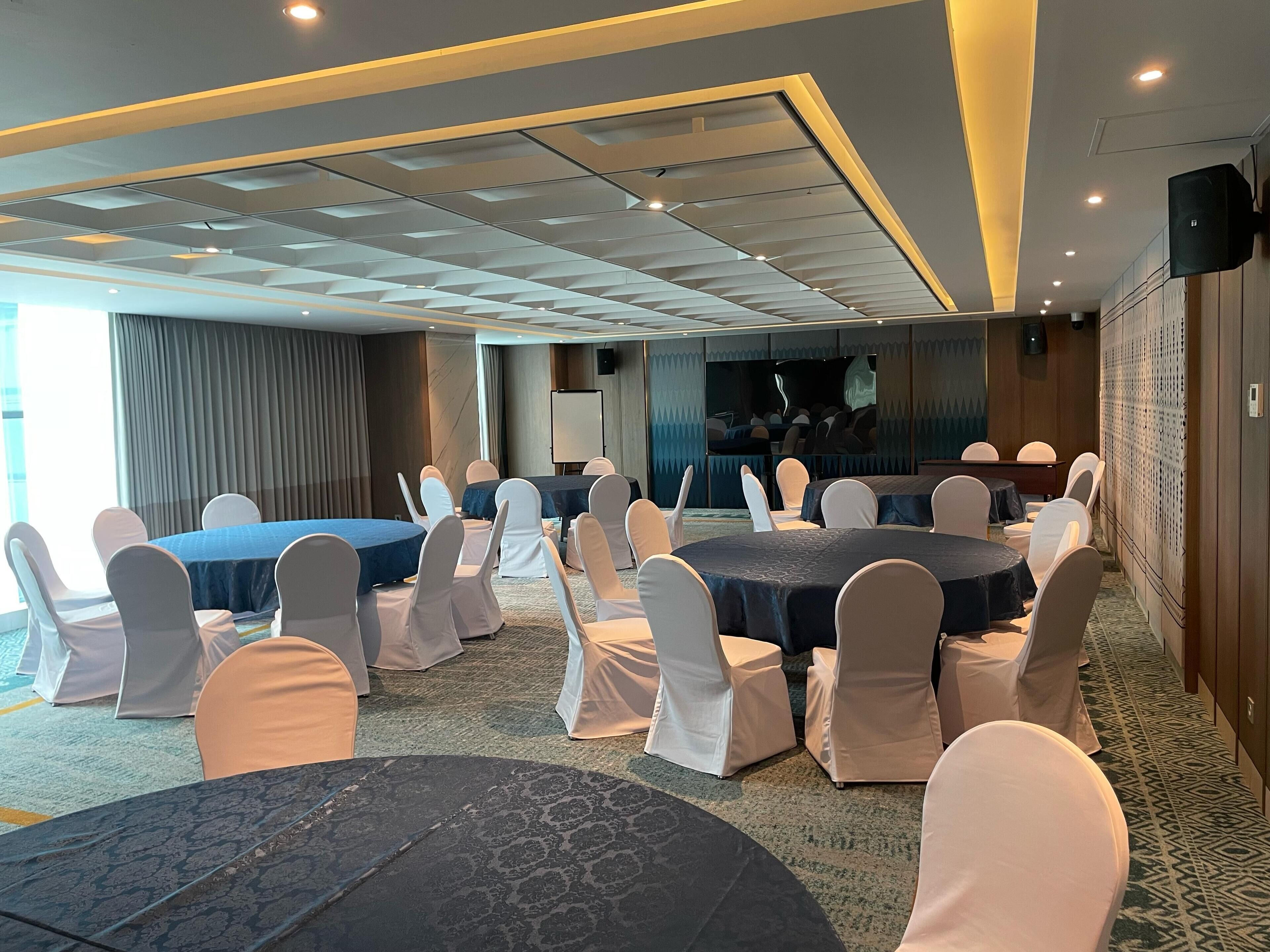 Un salón de conferencias con mesas y sillas redondas, una pantalla grande y una zona de escenario.