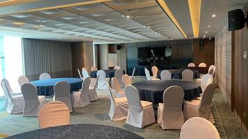 Un salón de conferencias con mesas y sillas redondas, una pantalla grande y una zona de escenario.