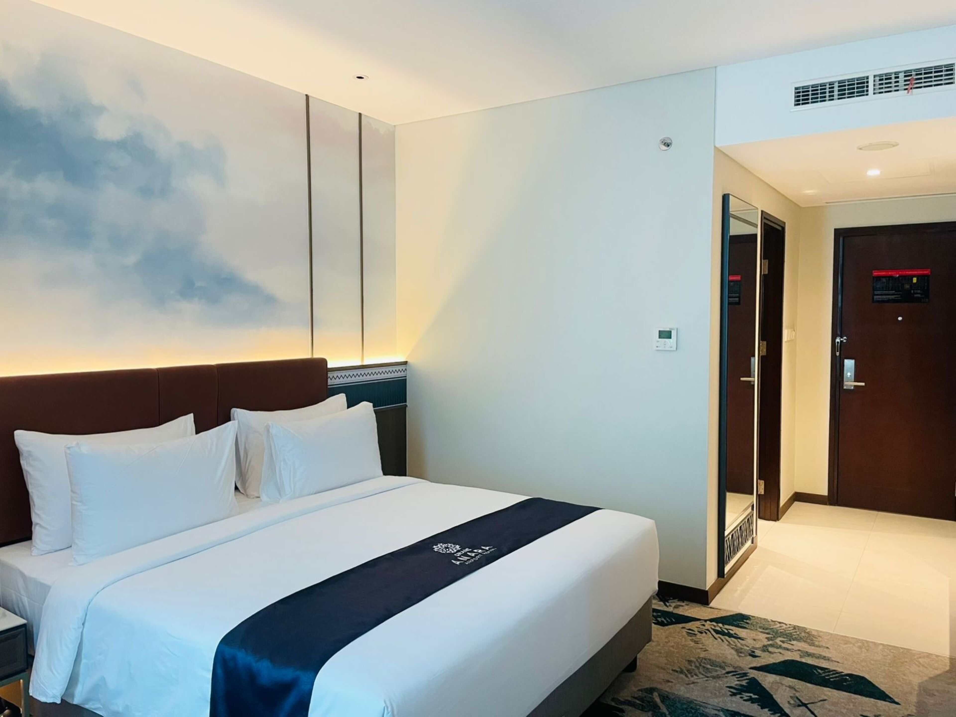 Hotelkamer met een groot bed, hoofdbord, een wandairconditioner, een deur met spiegel en een vloerbedekking.