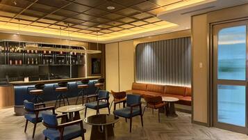 A modern bar area with a wooden floor, blue and brown seating, and a bar counter with bottles and glasses.