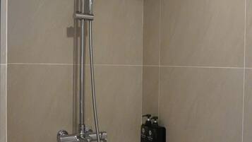 Une douche équipée d’un pommeau de douche à main et d’un robinet fixé au mur.