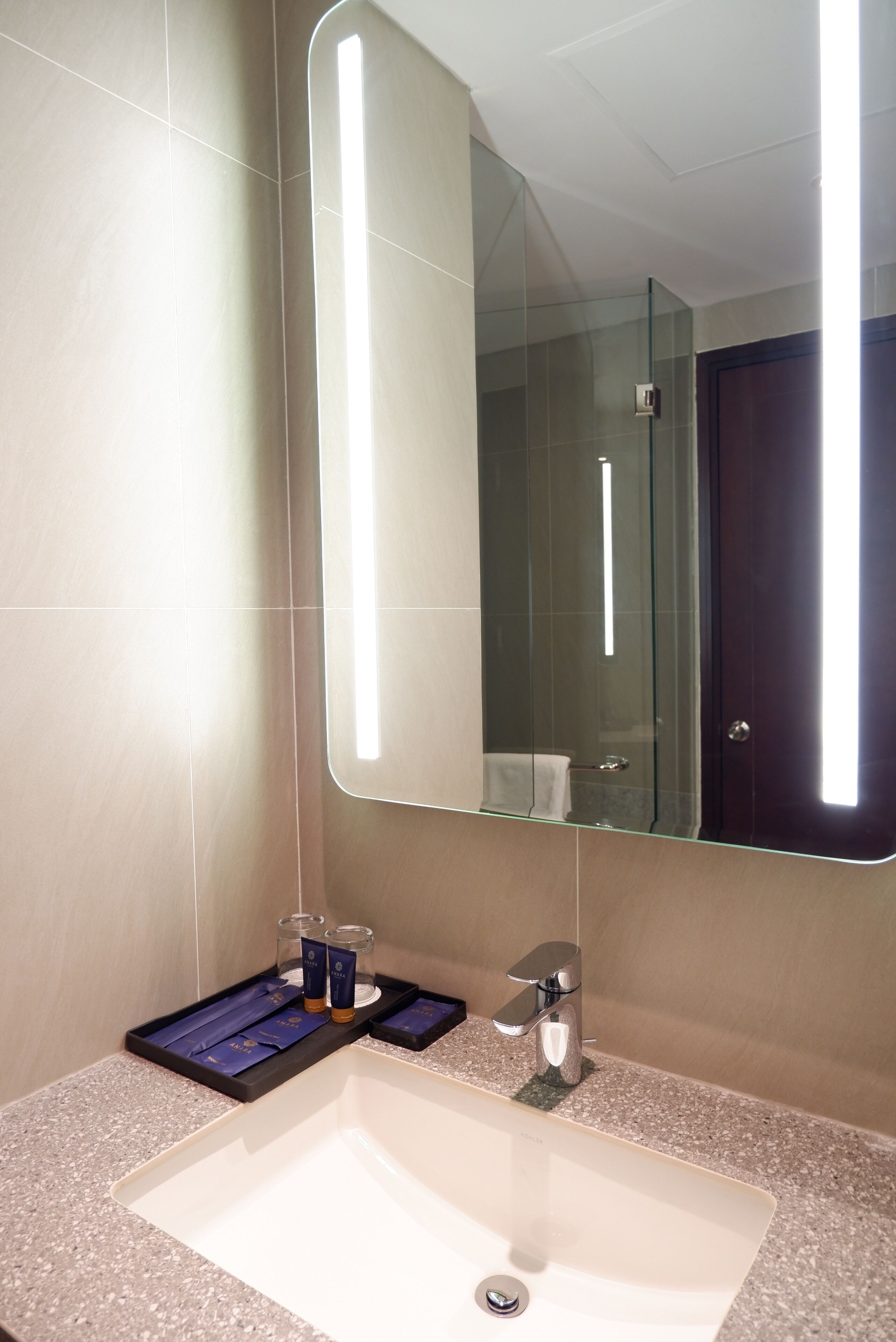 A modern bathroom with a large mirror, a sink, and a glass shower enclosure.