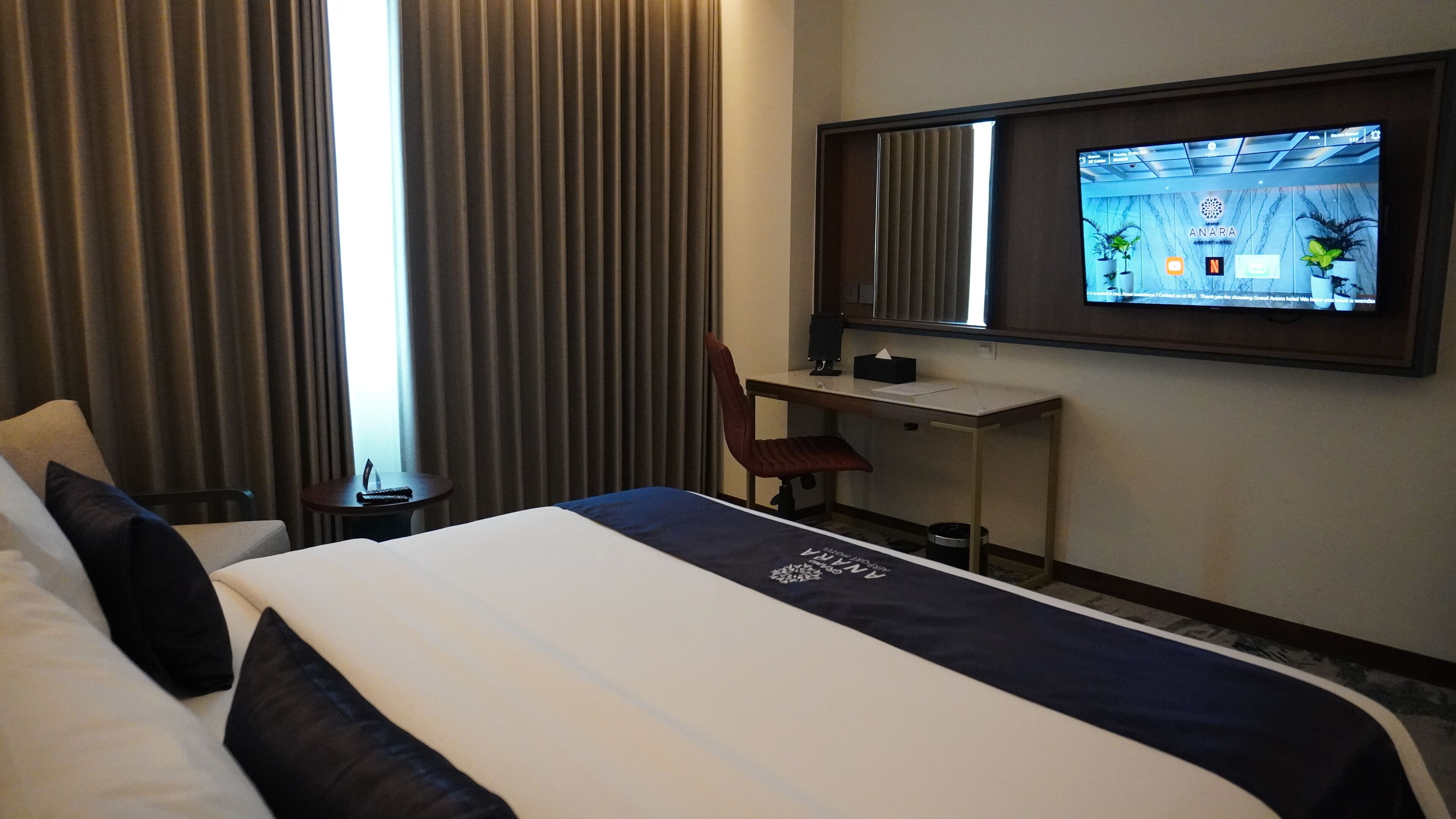 A hotel room with a bed, a desk, a chair, and a TV mounted on the wall.