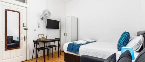 Une petite chambre comprenant un lit, un bureau, une chaise, une armoire et un téléviseur.