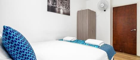 Ein Hotelzimmer mit Bett, Stadtbild-Poster, Kleiderschrank, Ventilator und Holztür.