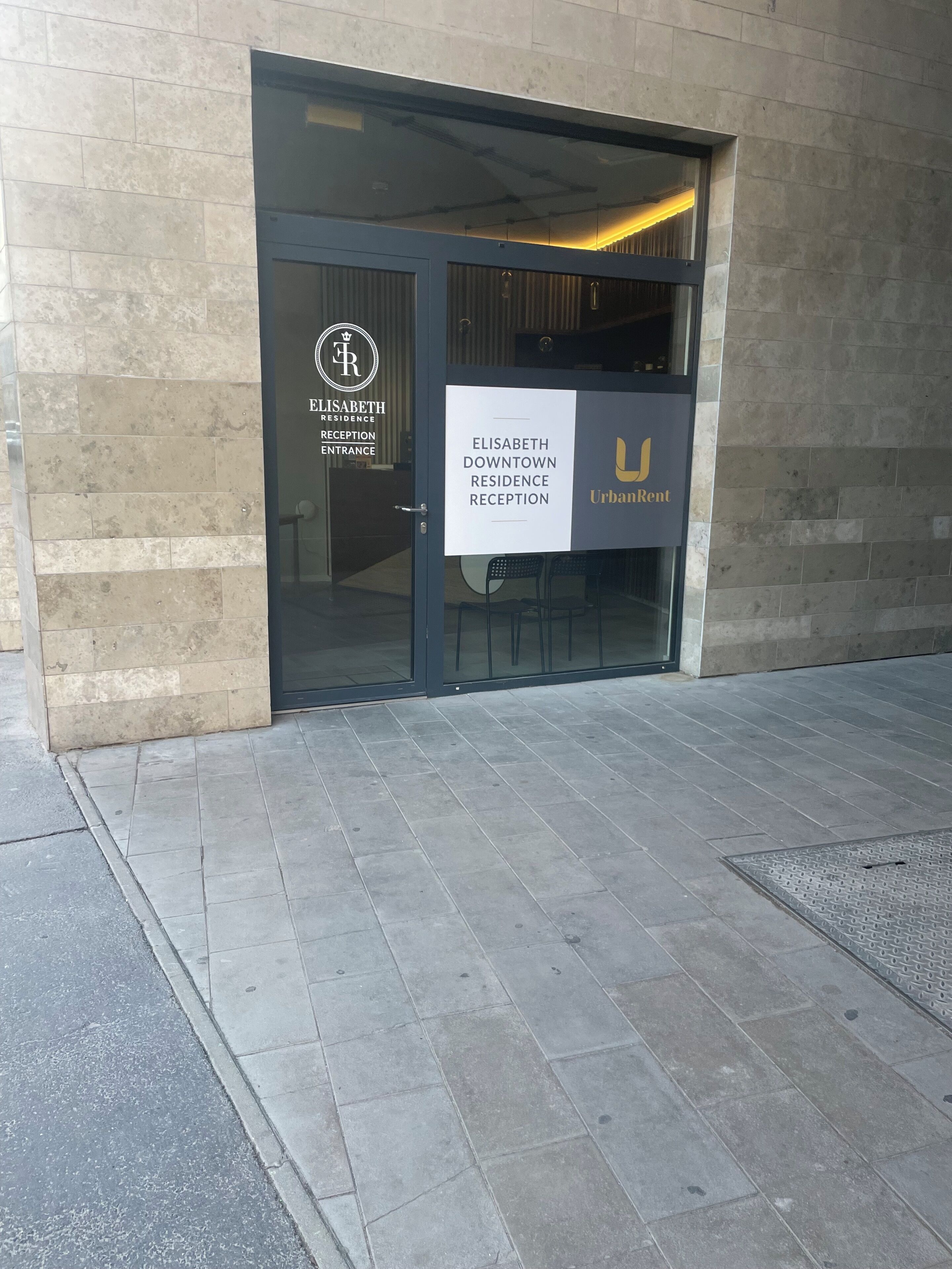 A building entrance with a reception desk labeled "Elisabeth Downtown Residence Reception" and "UrbanRent" signage.