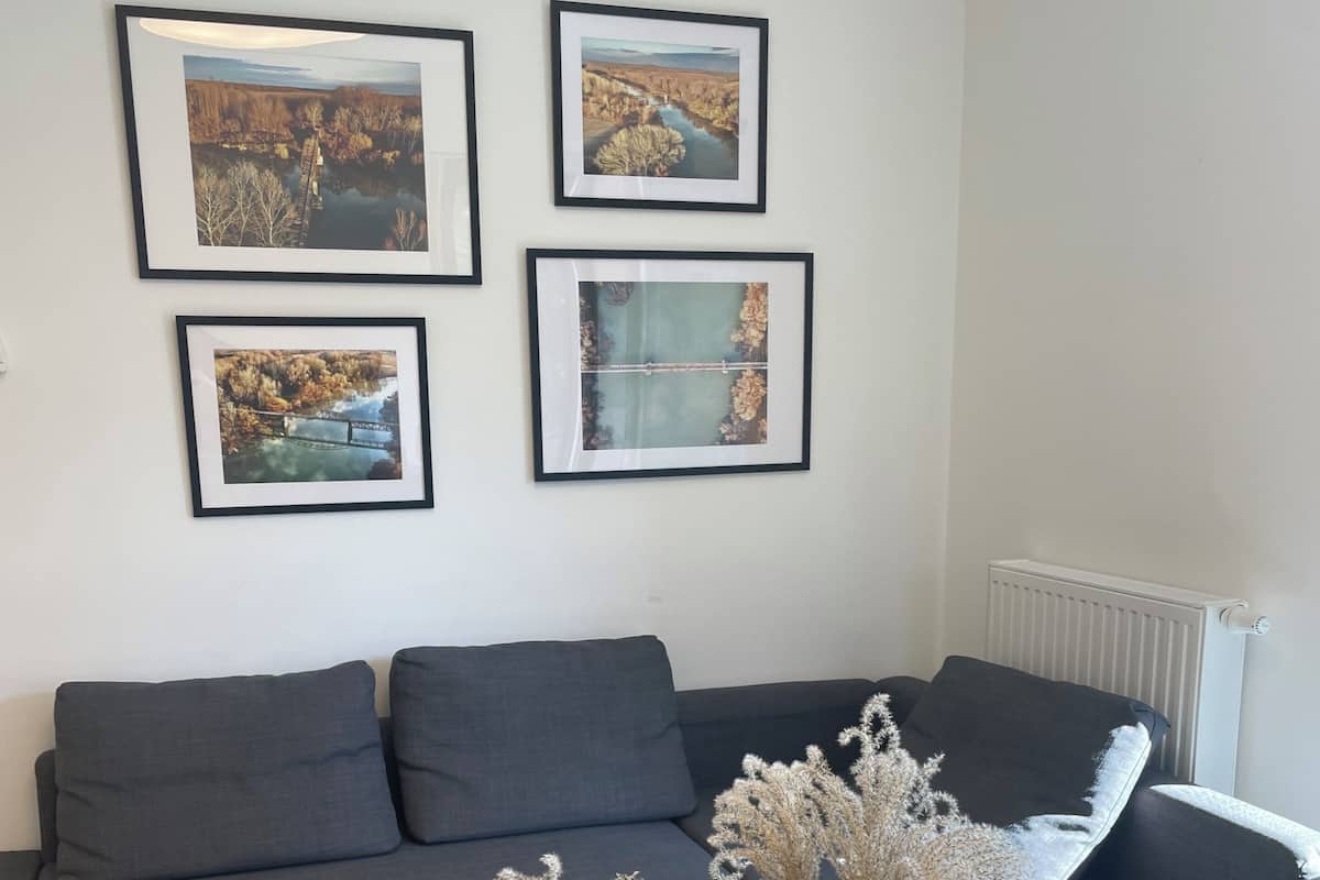 A modern living room with a grey sofa, a radiator, and four framed landscape photographs on the wall.