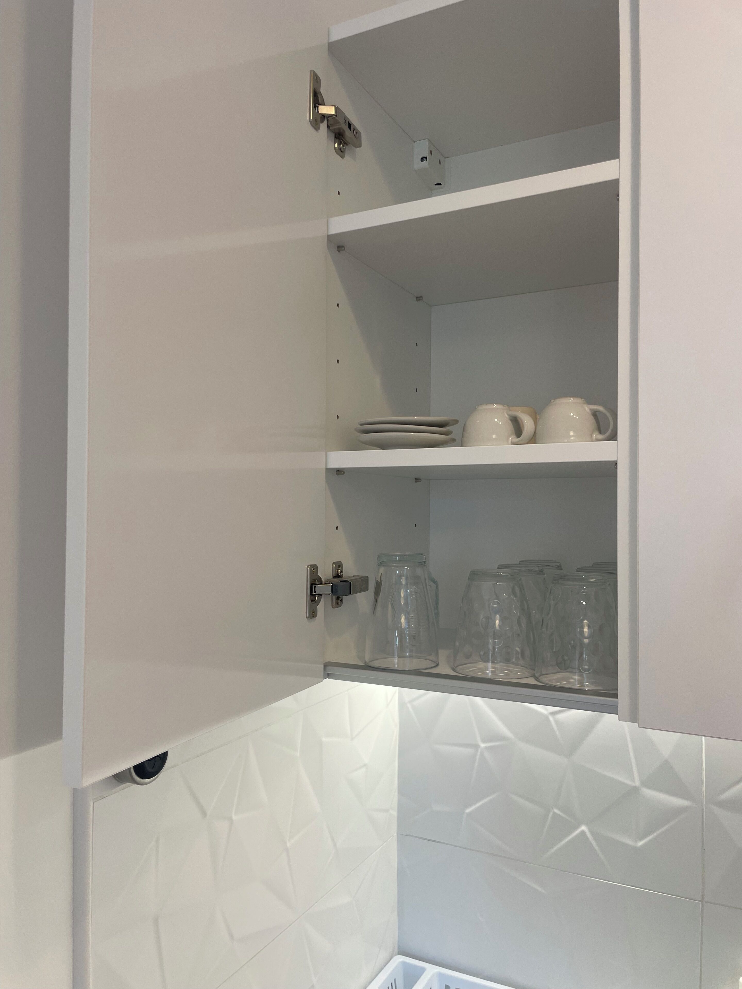 A white cabinet with shelves containing plates, cups, and glass jars.