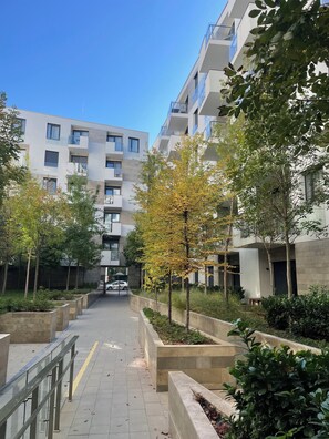 Een modern appartementencomplex met meerdere balkons, een centraal pad en omliggend groen.
