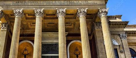 Une façade de style classique, ornée de colonnes corinthiennes et d’un fronton portant des inscriptions.