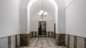 Un pasillo con piso de tablones, paredes blancas y una araña.