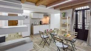 Una cocina moderna con armarios blancos, un comedor con mesa y sillas de madera, y una escalera con barandillas blancas.