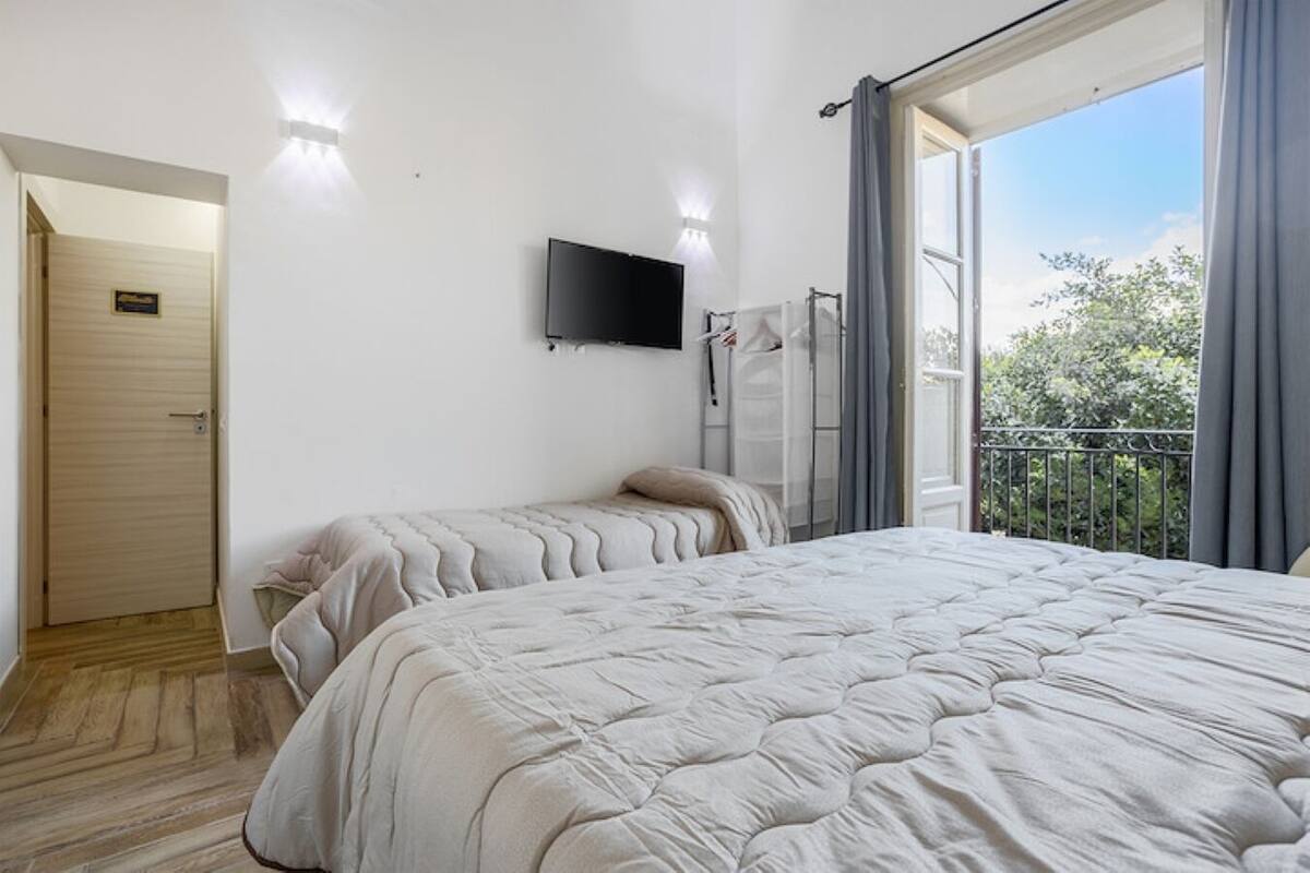 A bedroom with a large bed, a TV mounted on the wall, and a balcony with curtains.