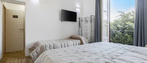 A bedroom with a large bed, a TV mounted on the wall, and a balcony with curtains.