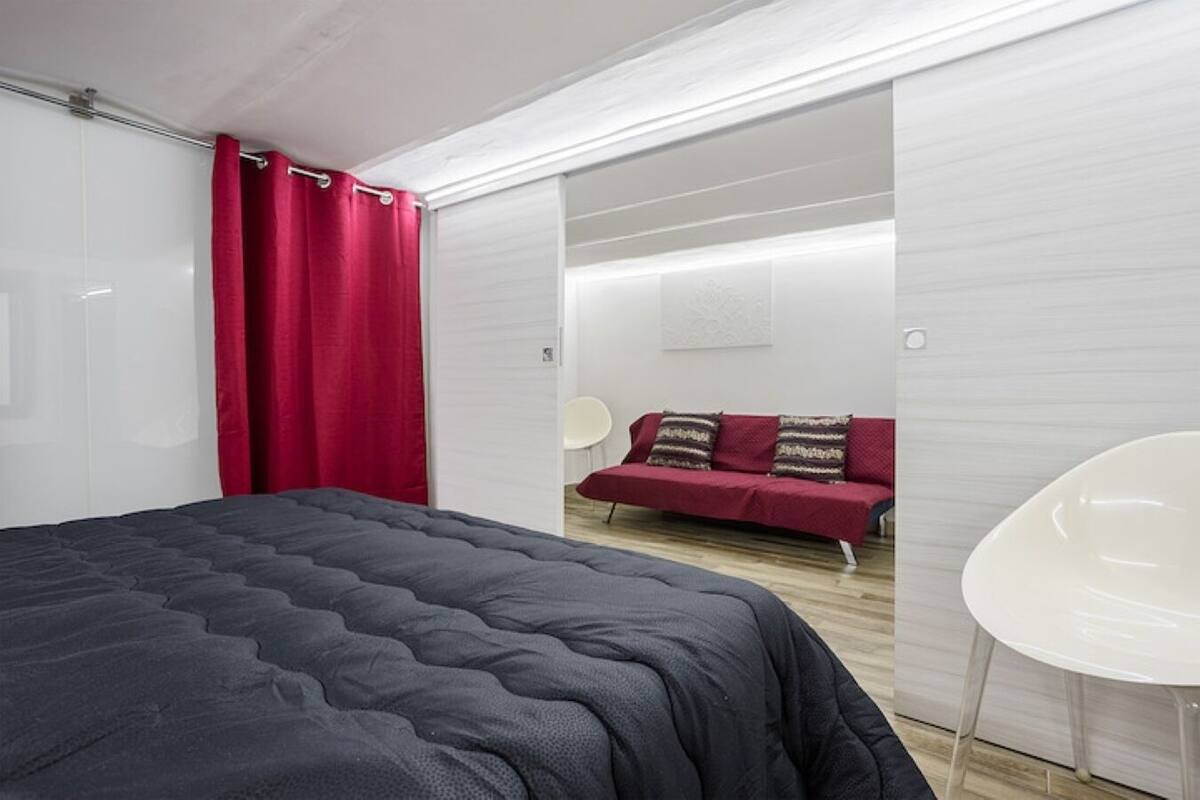 A modern bedroom with a large bed, a red sofa, and a white chair.