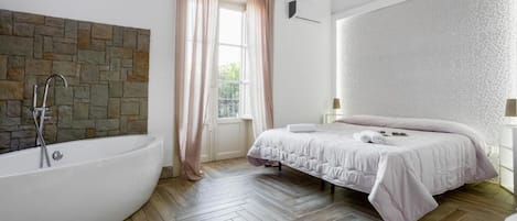 Un dormitorio con una bañera grande, una cama con edredón blanco y una pared de piedra.