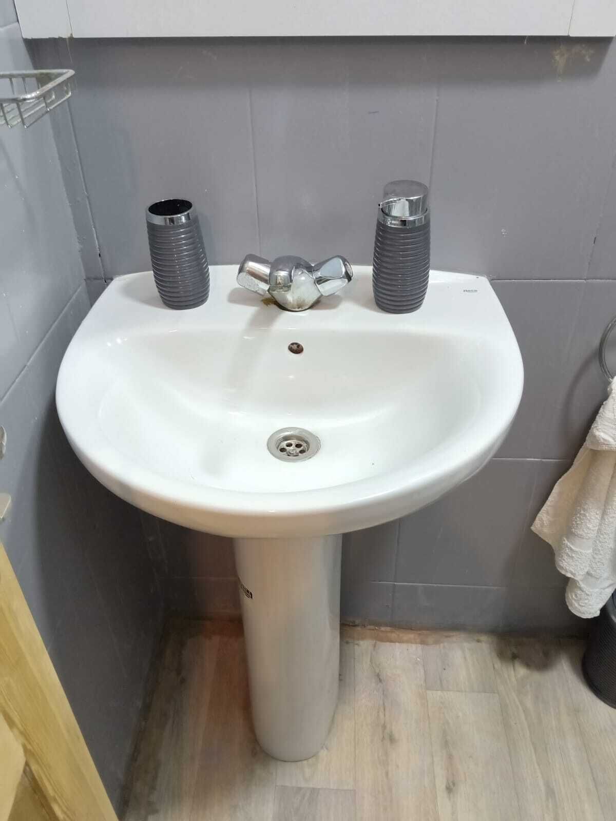 A white pedestal sink with two chrome faucets and a drain.