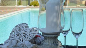 Un porte-bougie en verre, avec des bougies et des coquillages, est posé sur une table près d’une piscine.