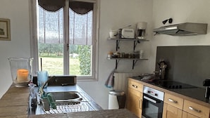 Une cuisine dotée d’un îlot central en pierre, d’appareils électroménagers en acier inoxydable et d’une fenêtre donnant sur un paysage verdoyant.