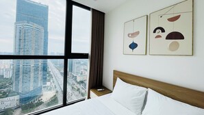 Hotellihuone, jossa on suuri ikkuna, josta avautuu näkymä kaupunkiin, siististi pedattu sänky ja seinällä abstraktia taidetta.
