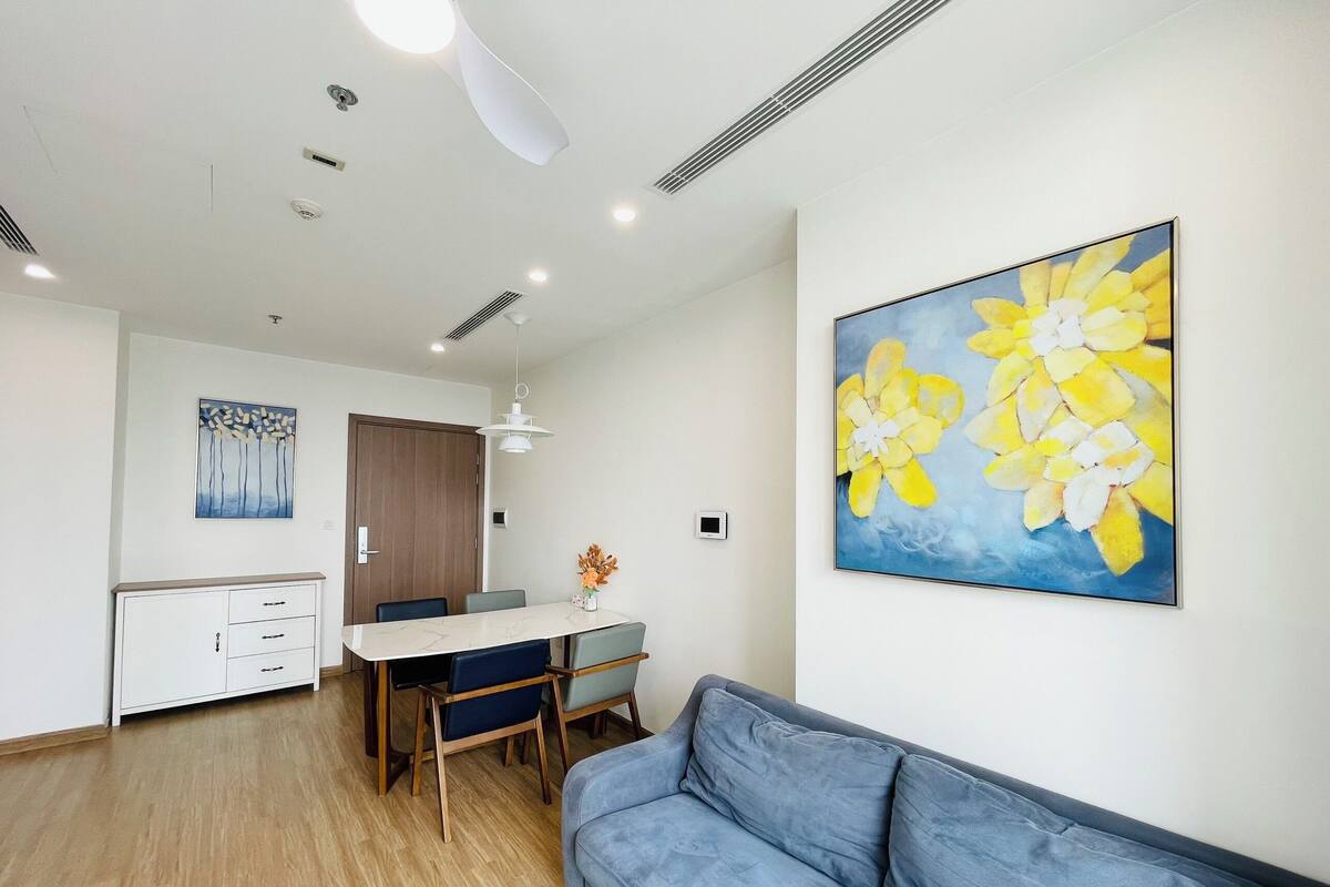 A modern living room with a blue sofa, a dining area with a white table and chairs, and a large floral painting on the wall.