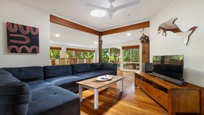 A modern living room with a sectional sofa, a wooden coffee table, a flat-screen TV, and a ceiling fan.