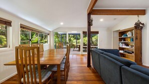 A spacious dining area with a long wooden table and chairs, a dark blue sofa, and a wooden bookshelf.