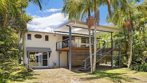 A modern house with a covered patio, a wooden deck, and a staircase leading to an upper level.